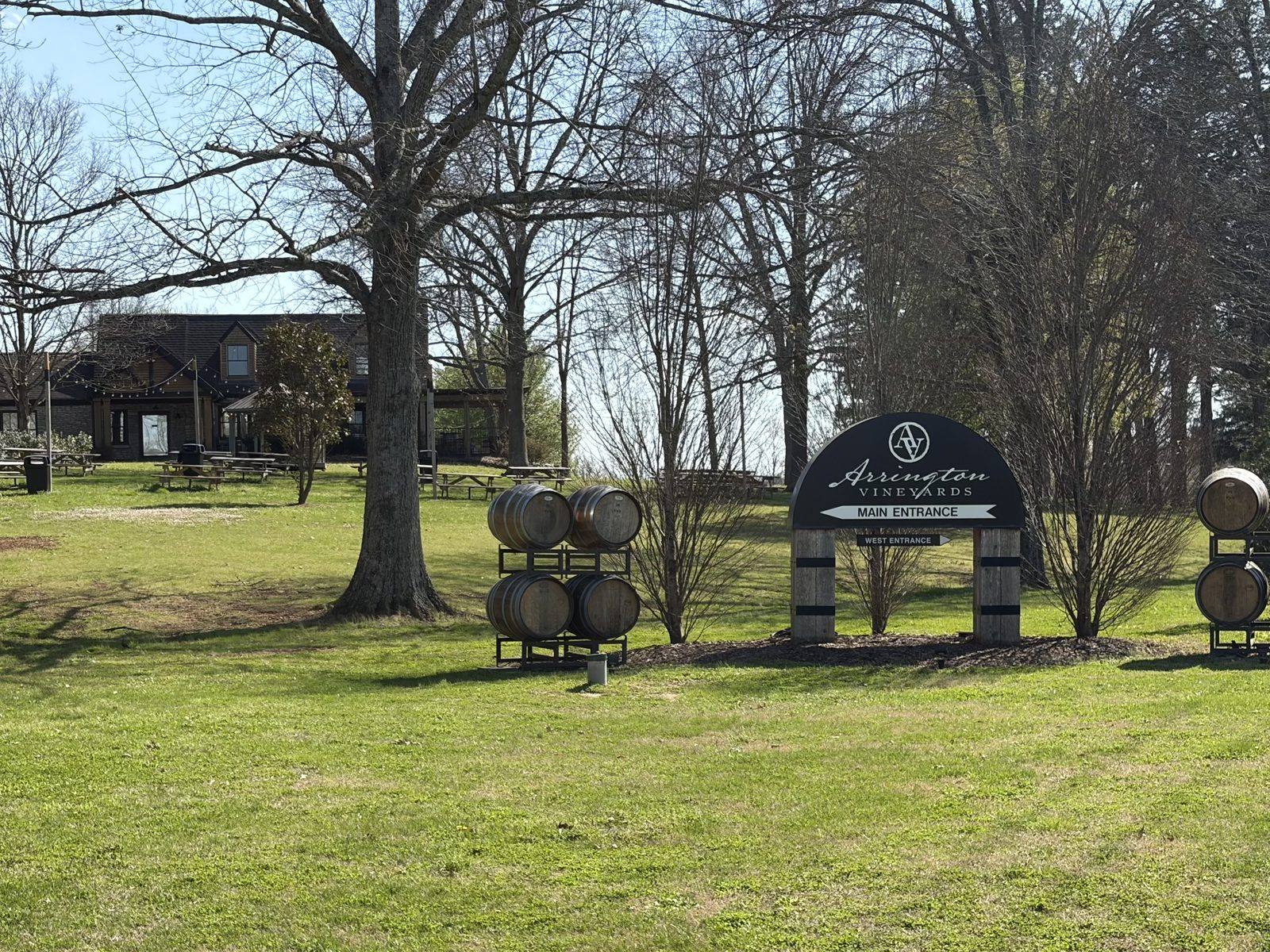 The lawn at Arrington Vineyards in early spring: picnic tables under bare hardwoods below a stone-and-timber tasting building