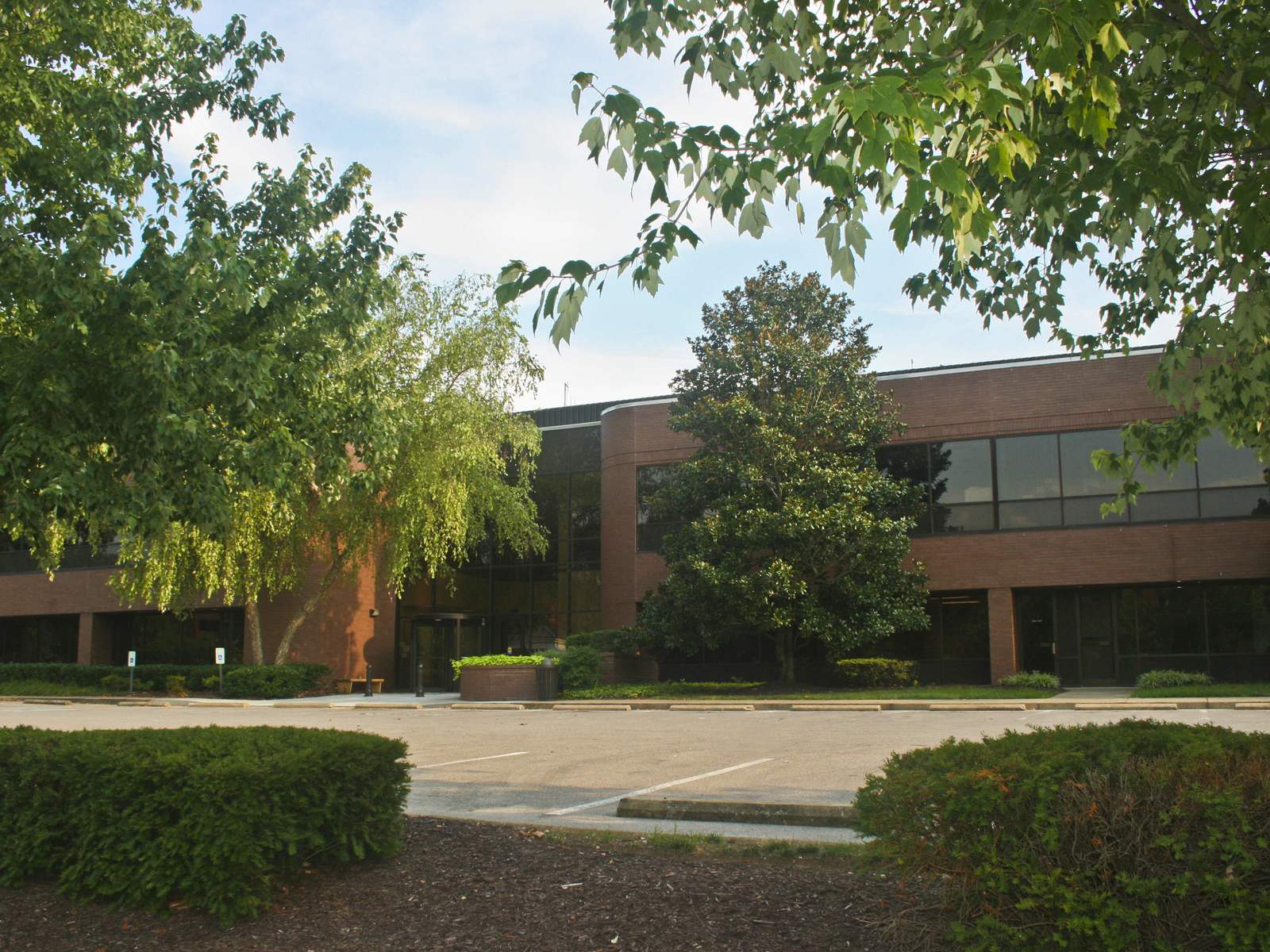 Brentwood City Hall, a two-story dark-brick office building with tinted windows, behind maples and a magnolia on Maryland Way