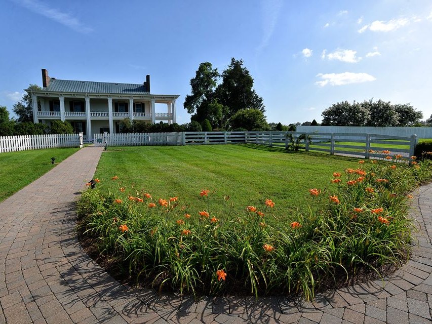 The front of Carnton, a two-story brick house with a white two-level porch, behind a lawn and a bed of daylilies