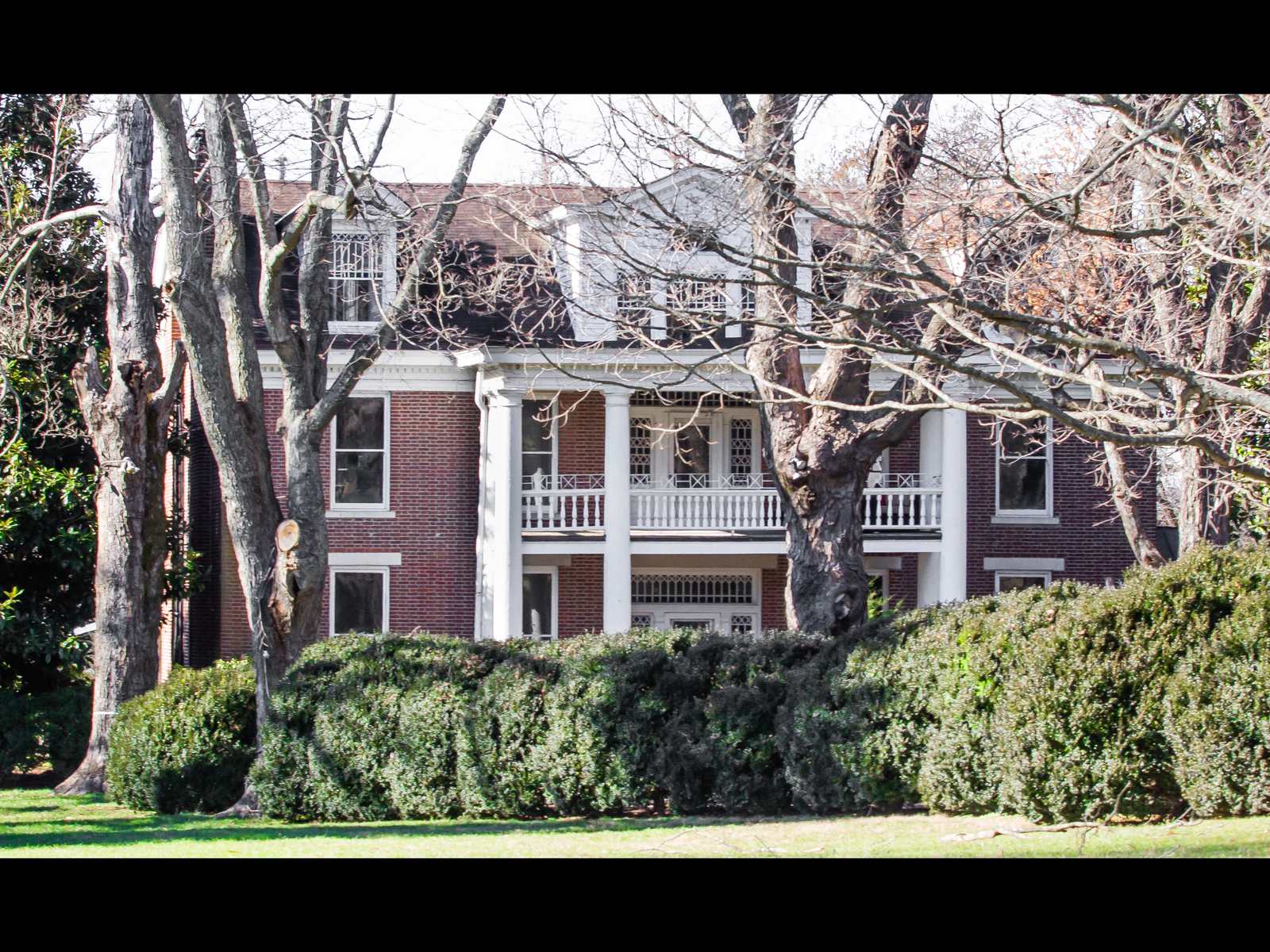A three-story red-brick Federal house with a white two-story portico and green shutters, seen across a winter lawn with bare trees